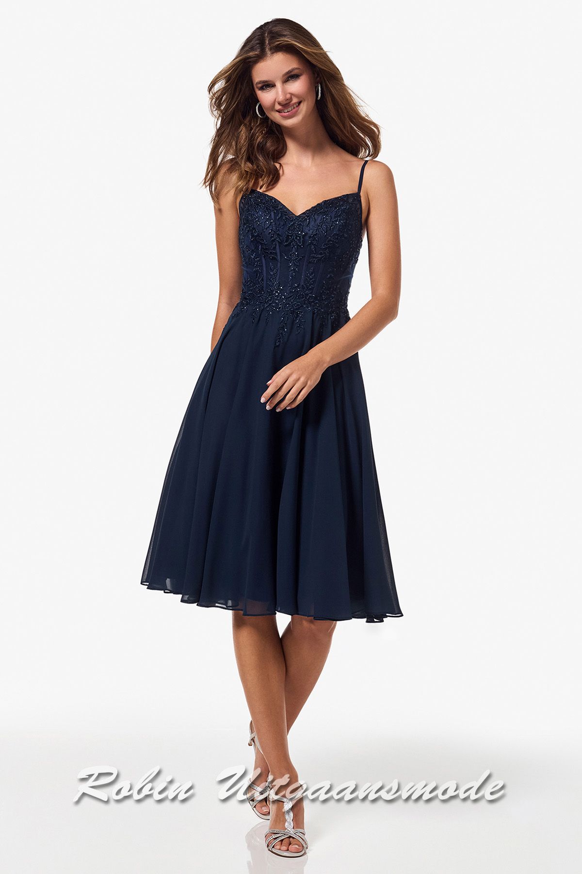 Korte navy blauwe galajurk met versierd kanten lijfje, smalle bandjes recht doorlopend over de open rug en licht geplooide chiffon rok tot net over de knie.