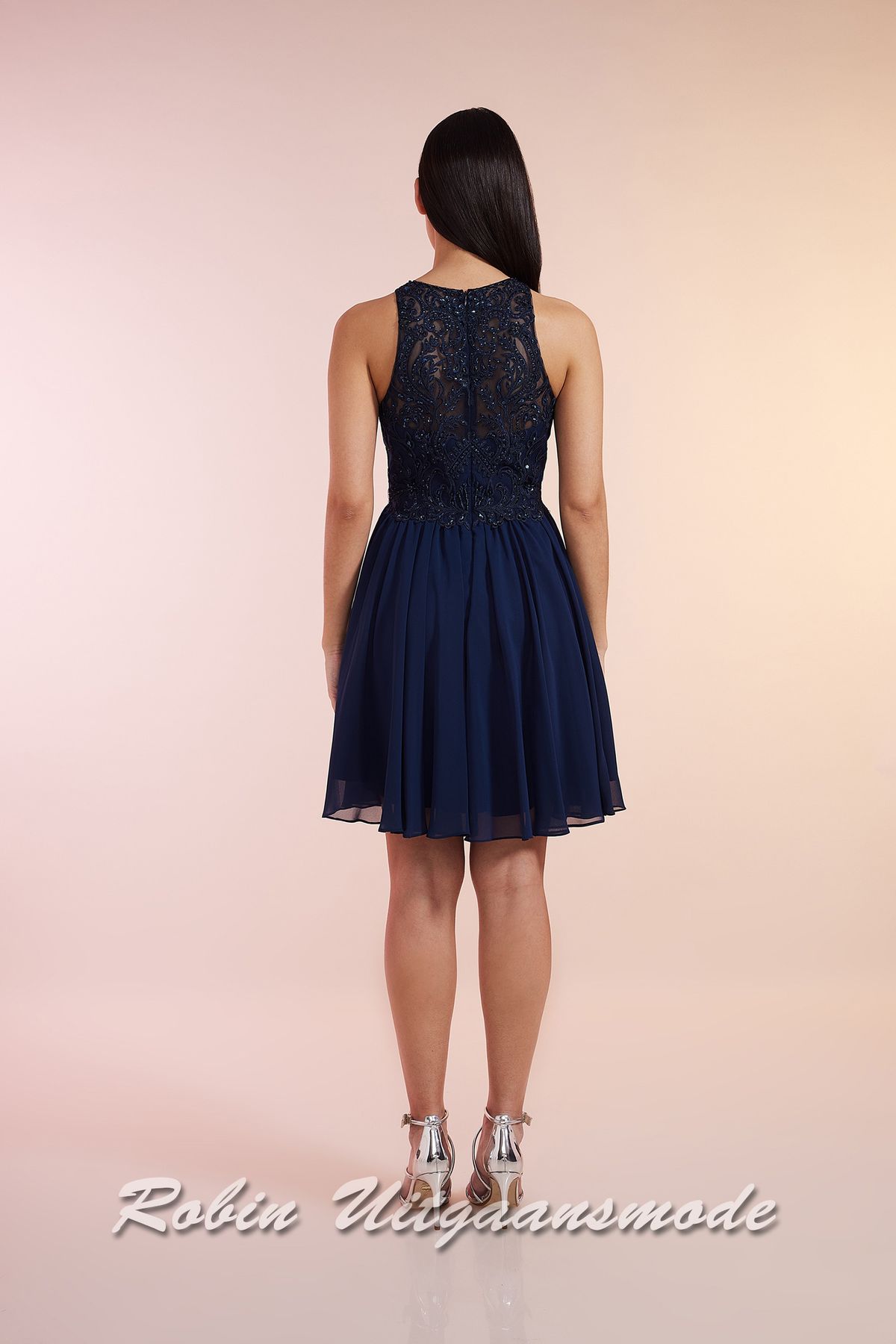 Achterkant van de Navy blauwe cocktailjurk met hooggesloten kanten lijfje, blote schouders en een geplooide chiffon rok tot net boven de knie