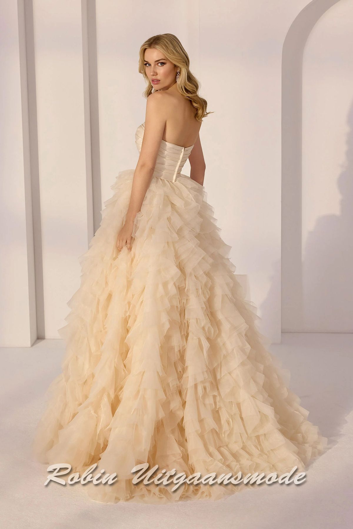 Achterkant van de Champagnekleurige baljurk met strapless lijfje met sweatheart hals lijn, gedrapeerd satijnen en een geplooide A-lijn rok met een cascade van lagen tule en organza