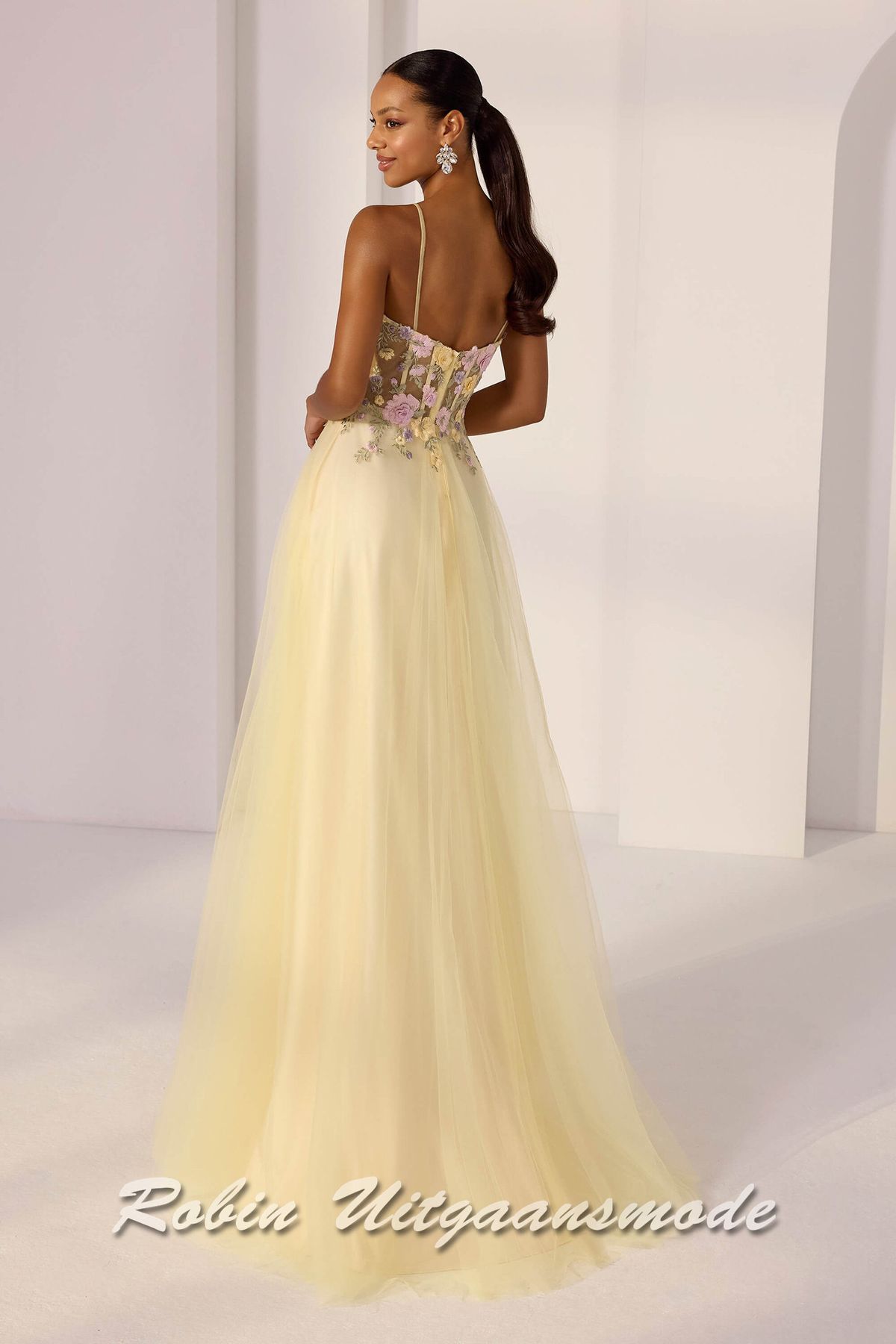 Achterkant van de Gele A-lijn galajurk met geborduurde bloemen in het roze, lila en geel op de korset top, een heartshape bustelijn en wijduitlopende rok met tule toplaag.