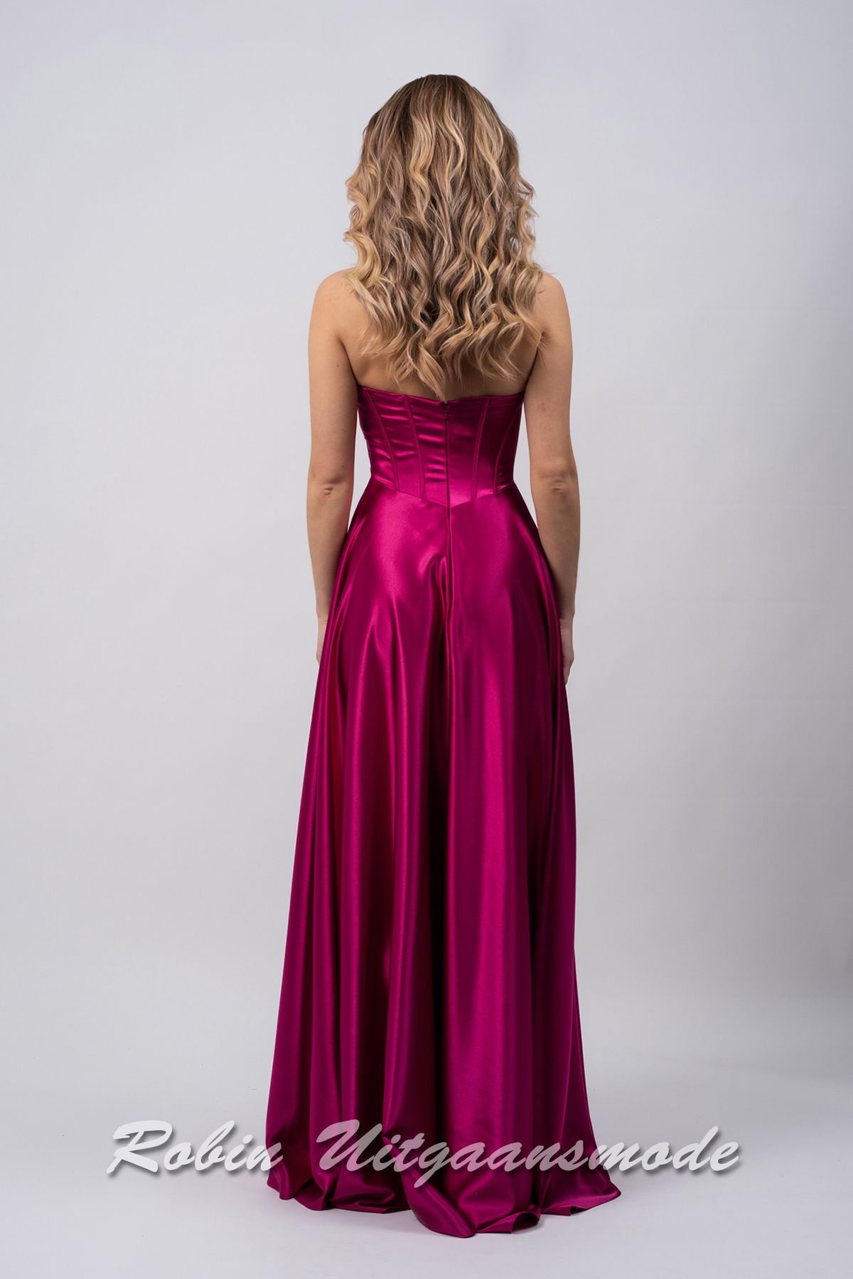 Achterkant van de Magenta avondjurk met strapless asymmetrische halslijn, brede banden schuin over de buste lopend naar de linkertaille en licht geplooide rok tot op de grond