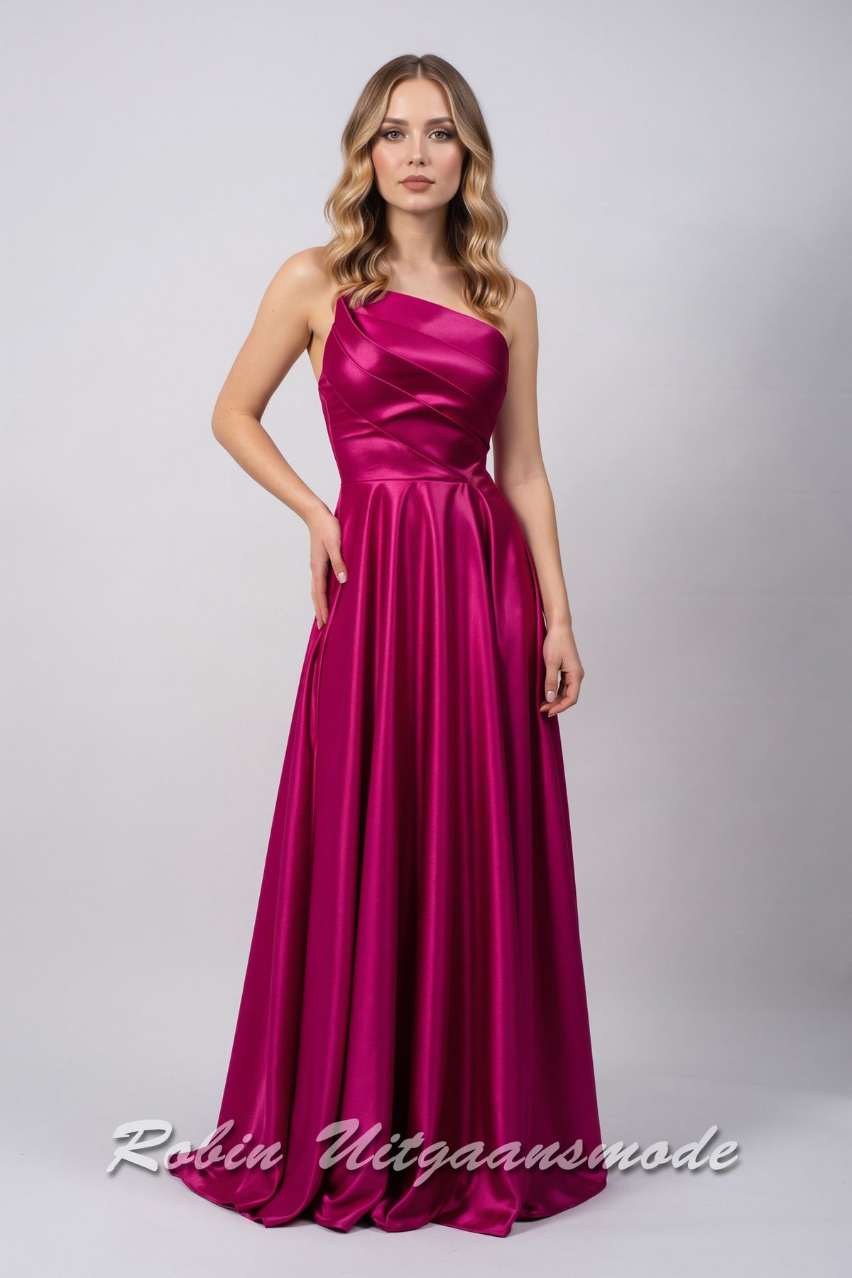 Magenta avondjurk met strapless asymmetrische halslijn, brede banden schuin over de buste lopend naar de linkertaille en licht geplooide rok tot op de grond