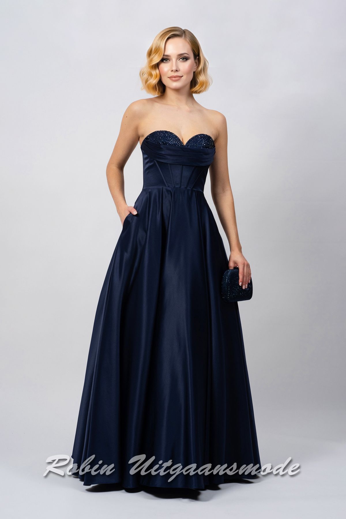 Strapless inktblauwe avondjurk met A-lijn rok, een heartshape bustelijn versierd met sprankelende pailletten en afgewerkt met waterval band