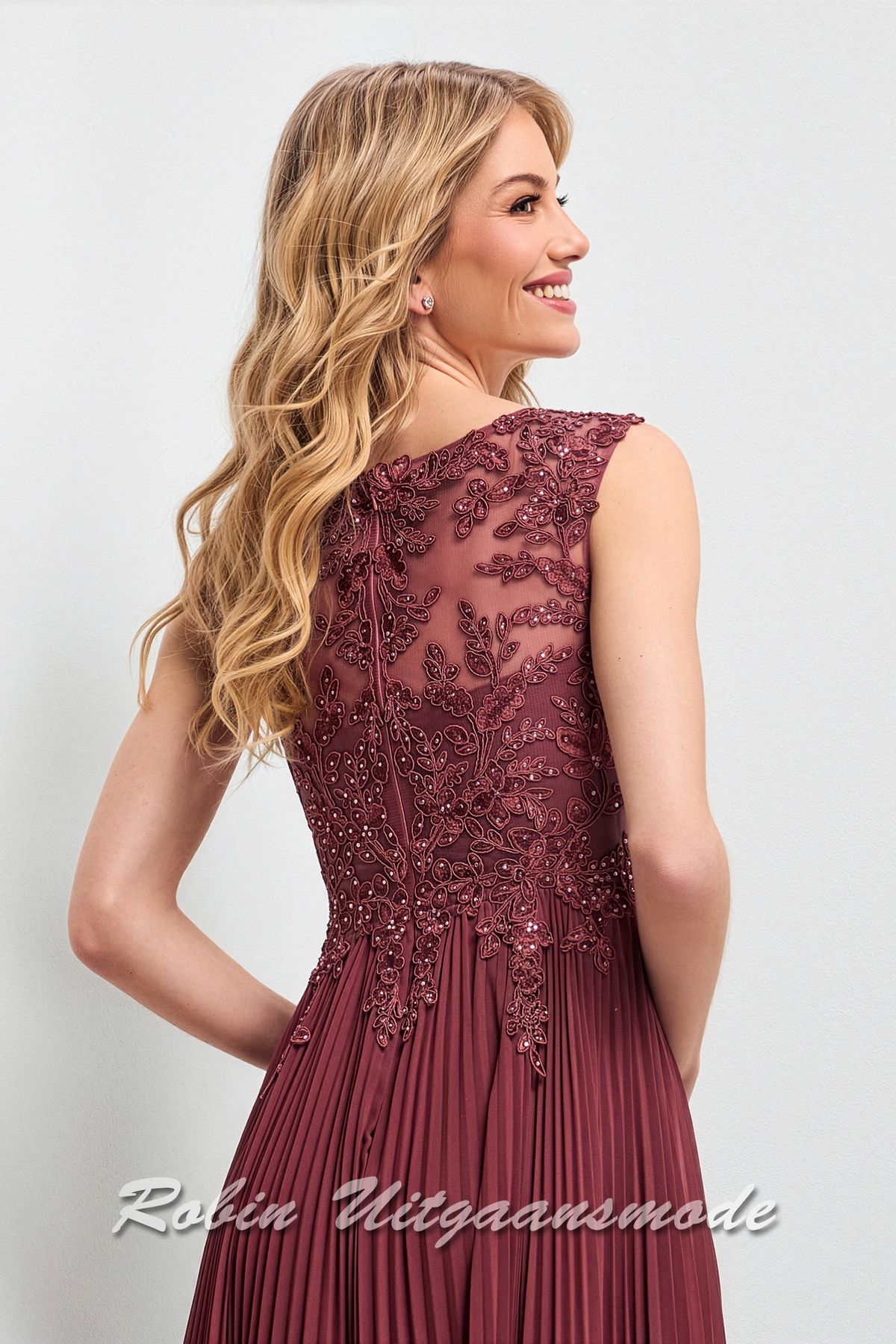 Close-up van de hooggesloten rug van de Deftige steenrode avondjurk met kanten lijfje, boothalslijn, blote schouders en een chiffon plissé rok met lengte tot op de grond