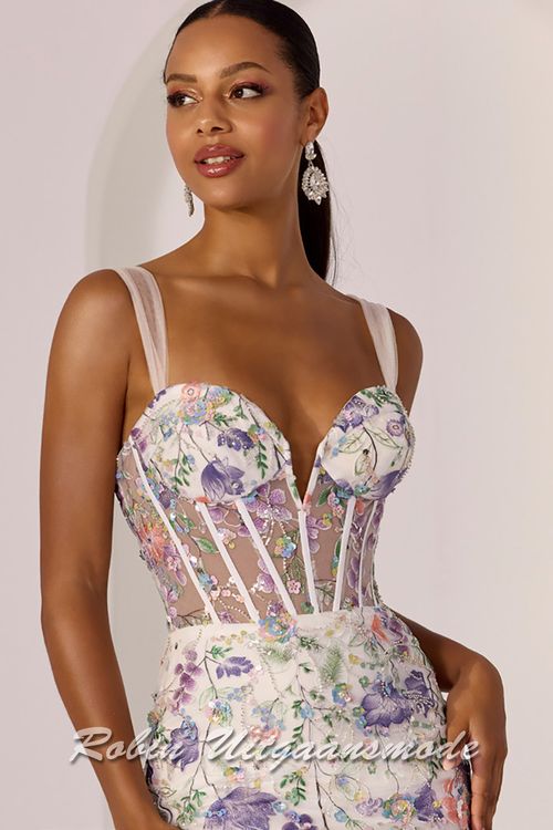 Close-up van de Ivoorkleurige galajurk volledig versierd met geborduurde bloemen, pailletten, een korset lijfje met diep uitgesneden bustelijn, lange rok met hoge split