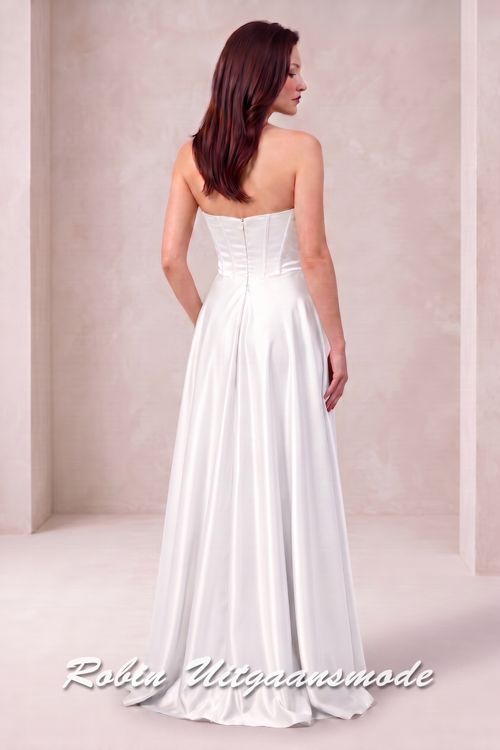 Achterkant van de Trouwjurk met strapless asymmetrische halslijn, brede banden schuin over de buste lopend naar de linkertaille en licht geplooide rok tot op de grond