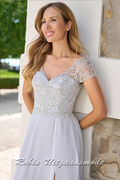 Close-up van de Zilvergrijze  lange avondjurk met kanten lijfje versierd met sprankelende steentjes, kapmouwtjes en chiffon rok met split